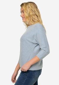 Stribet blå og hvid top med rund halsudskæring, letvægtsstof, trekvartærmer og et afslappet fit, parret med mørk denimjeans.