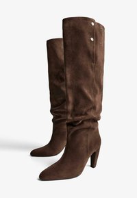 Brązowe zamszowe botki do kolan z wysmukłym czubkiem, smukłym obcasem i dekoracyjnymi napami na górze, o miękkim, teksturowanym wykończeniu.