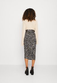 Jupe midi noire avec un motif d'étoiles blanches et dorées, présentant une taille cintrée et un pull en tricot texturé beige, porté avec des sandales à talons épais.