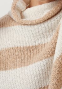 Beige och krämrandig stickad tröja med hög cowl-hals. Mjuk textur, med växelvisa breda ränder i olika nyanser.