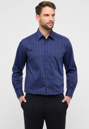 Chemise habillée bleu marine avec des rayures verticales en bleu, rouge et blanc. Dotée d'une fermeture boutonnée sur le devant, d'un col pointu et d'une poche simple sur la poitrine.