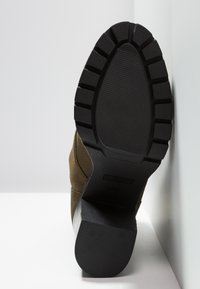 Bruine suède enkellaars met een gestructureerde zwarte rubberen zool. Het profiel toont een stevige ontwerp, met een diep profiel en platte hak voor stabiliteit.