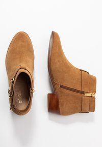 Tan suede ankle boots with a pointed toe, side zip, and gold hardware accents. Features a stacked wooden heel for stability.