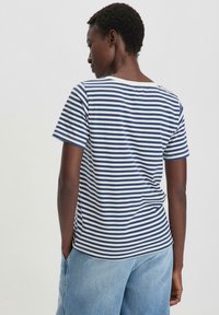 Gestreiftes T-Shirt mit navyblauen und weißen horizontalen Streifen, kurzen Ärmeln, Rundhalsausschnitt und weichem Stoff, kombiniert mit hellblauen weiten Jeans.