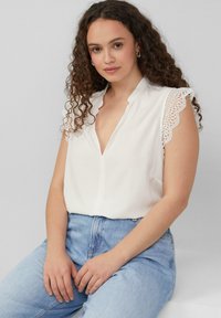 Blouse blanche avec un décolleté en V profond et des manches en dentelle festonnées, assortie à un jean en denim bleu clair taille haute. Tissu lisse avec une coupe décontractée.