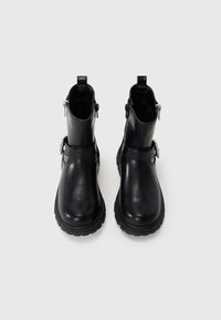 Bottines en cuir noir avec une texture lisse, fermeture éclair et détail de boucle sur le côté, dotées d'une semelle en caoutchouc épaisse pour une meilleure traction.