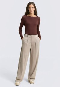 Braunes langärmeliges Oberteil kombiniert mit hoch taillierter beige weiter Hose. Der Stoff wirkt glatt; die Hose besitzt vordere Falten und Taschen.