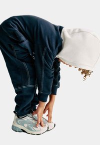 Marineblauwe hooded trainingspak met witte accenten, voorzien van elastische manchetten en gestikte details. Lichtgewicht, stevige sneakers met mesh en lichtblauwe accenten.