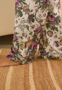 Pantaloni da pigiama floreali in misto seta, con rose viola e gialle su fondo bianco, dalla vestibilità comoda e dalla texture morbida.