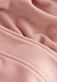 Blødt pink stof med en glat overflade og subtil ribbet mønster. Indeholder en sømdetalje langs kanten, der skaber dimension.