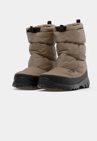 Bottes rembourrées marron avec un design matelassé, dotées de semelles et d'accents en caoutchouc noir, de poignets ajustables et d'un bout arrondi et rembourré.