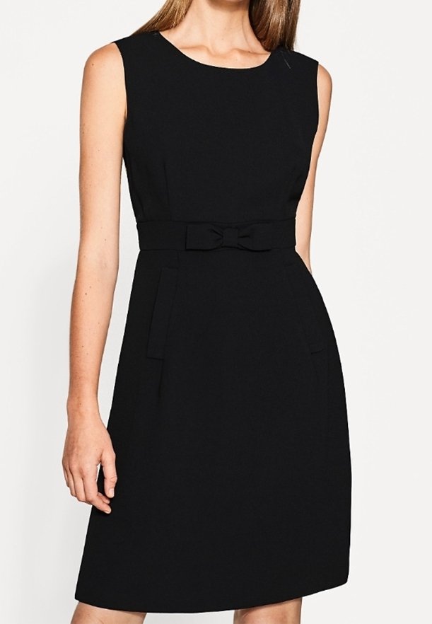 Robe noire sans manches longueur genou avec un col rond et une ceinture en tissu nouée en petit nœud à la taille.