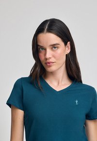 Grön V-ringad t-shirt i mjuk bomull, med korta ärmar och en liten broderad logotyp på bröstet. Slät textur.