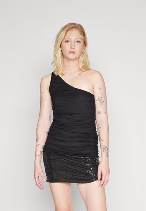 Μαύρο τοπ με έναν ώμο από ελαστικό υλικό με ρυτιδωμένη λεπτομέρεια, συνδυασμένο με μαύρη μίνι φούστα με πούλιες που αντανακλά το φως.