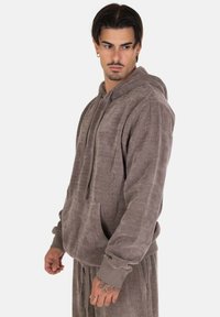 Hoodie in velluto a coste marrone con tasca frontale, cappuccio con cordoncino e polsini a coste. Tessuto morbido e vestibilità casual, abbinato a pantaloni coordinati.
