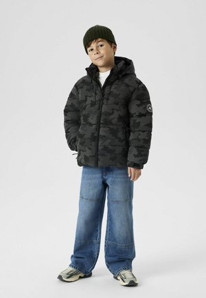 Doudoune camouflage noire avec fermeture éclair à l'avant, grandes poches et capuche. Associée à un jean en denim bleu ample et des baskets aux tons neutres.