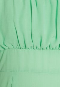 Tecido verde menta com uma textura suave e macia. Detalhes franzidos na cintura, criando um efeito fluido. Design simples e despretensioso.