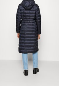 Mörkblå puffjacka med huva, åtsittande midja och horisontell quiltning. Kombinerad med ljusblå jeans och svarta ankelstövlar.