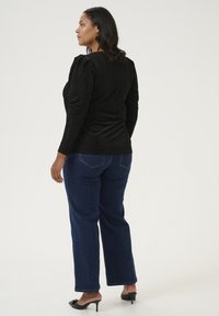 Schwarzes, geripptes Longsleeve-Oberteil mit puffigen Schultern, kombiniert mit dunkelblauen geraden Jeans und schwarzen offenen High Heels.