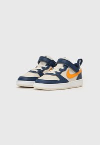 Baskets Nike avec un dessus en cuir bleu marine et crème, un swoosh orange, une sangle velcro, une pointe perforée, et une semelle en caoutchouc blanc.