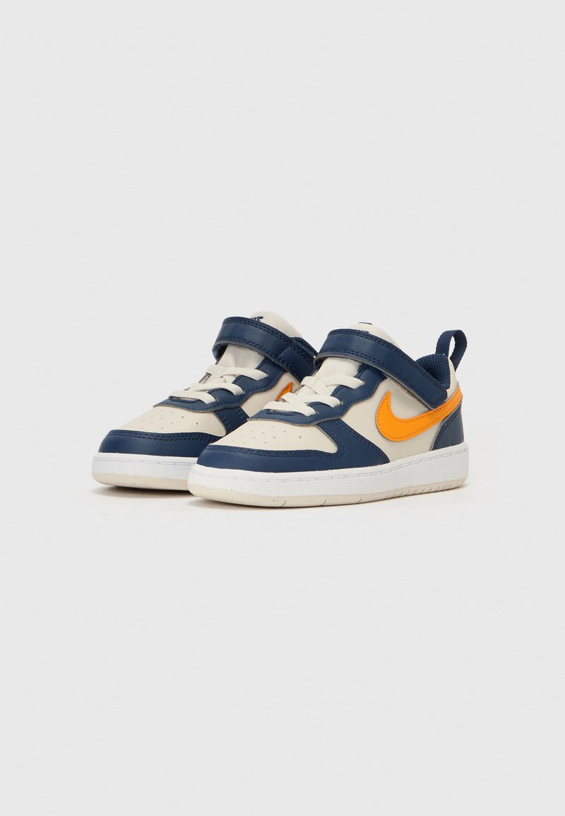 Sneakers Nike z cholewką z granatowego i kremowego skóry, pomarańczowym logo Swoosh, rzepem, perforowanym noskiem i białą gumową podeszwą.