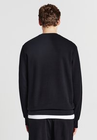 Felpa nera con tessuto a trama, maniche lunghe e polsini a costine. Caratterizzata da un semplice collo rotondo e un orlo dritto in vita.