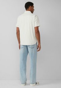 Korte mouwen, lichtbeige shirt met een achterste yoke-detail, gecombineerd met loszittende, lichtblauwe jeans en witte sneakers met grijze accenten.