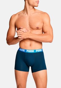 Marineblaue Boxershorts mit weicher Textur und einem hellblauen Puma-Logo am Bund. Das Design zeichnet sich durch eine figurbetonte Passform für Komfort aus.