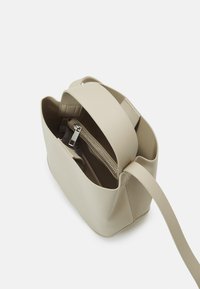 Piccola borsa a tracolla in pelle beige con una texture liscia, forma rettangolare e tracolla regolabile. Presenta una tasca con zip all'interno.