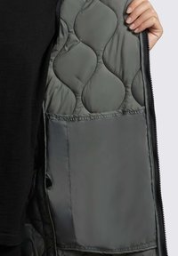 Quilted gray jacket interior with a smooth texture, featuring a pocket and black zipper. Visible stitch pattern adds dimension.