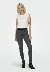 T-shirt blanc avec dentelle, jeans skinny gris foncé et bottines noires. Design simple avec une silhouette ajustée et un style minimaliste.