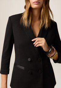 Blazer doppio petto nero su misura realizzato in tessuto liscio, con revers a punta, due bottoni e tasche laterali discrete.