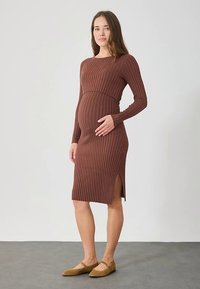 Brun ribbstickad mammaklänning med långa ärmar, figurnära siluett, sidsprund och mjuk textur, kombinerad med ljusbruna platta skor.