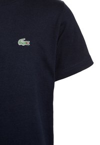 Mörkblå bomull t-shirt med en liten grön och röd krokodil-logga på bröstet, kort ärm och rund hals.