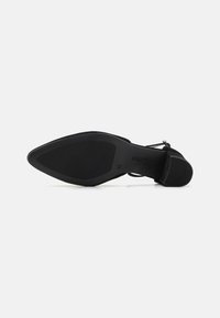 Black high-heeled shoe with a pointed toe and a smooth matte texture. Features a textured sole and an ankle strap with a buckle.