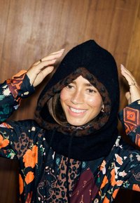 Fekete kapucni barna polár béléssel, színes, virág- és állatmintás ingezzel viselve. Simogató textúra.