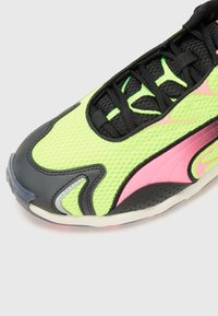 Adidași sintetici de culoare verde neon, cu accente negre, textură din plasă, detaliu lateral cu logo roz și talpă din cauciuc cu un finisaj ușor transparent.