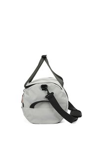 Sac de sport gris de forme ronde, fabriqué en tissu durable. Il comprend une bandoulière noire, des poignées latérales et un crochet de sécurité sur le côté.