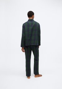 Set di pigiama a quadri con una base blu navy e un motivo a scacchi verdi. La maglietta a maniche lunghe e i pantaloni hanno una vestibilità ampia e una consistenza morbida.