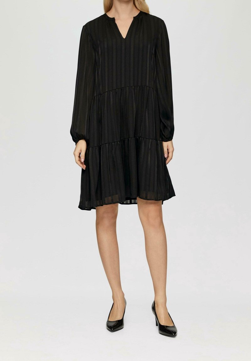 Černé šaty s volány, dlouhými rukávy a výstřihem do V, zdobené vertikálními pruhy a vzdušnou siluetou, vyrobené z lehkého, průsvitného materiálu.