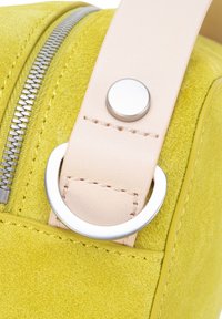 Geel suède tas met een licht lederen riem, zilverkleurige metalen details en een zichtbare ritssluiting aan de bovenkant. De textuur oogt zacht en glad.