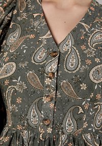Vestido verde con estampado floral y diseño de paisley, escote en V, y botones marrones en el frente, con una tela texturizada y dobladillo fruncido.