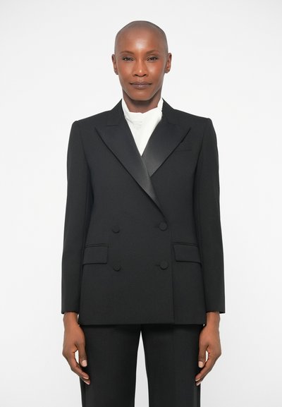 Schwarzer doppellagiger Blazer mit schmalen Revers, aus glattem Stoff. Verfügt über zwei Fronttaschen und passende schwarze Hosen.
