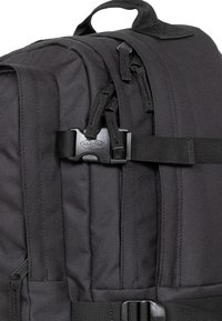 Black backpack made of durable fabric, featuring multiple zippers, adjustable straps, and a plastic buckle. Textured surface with reinforced seams.