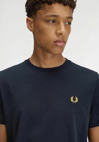 Camiseta azul marino de algodón, con cuello redondo y mangas cortas, adornada con un pequeño logotipo bordado amarillo en el pecho.