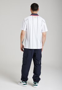 Polo bianco con righe verticali nere e colletto blu navy. Abbinato a pantaloni cargo blu navy con tasche laterali e sneaker bianche con dettagli verdi.