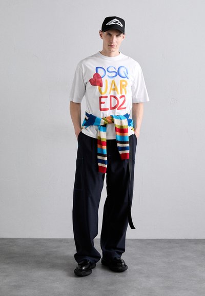 T-shirt blanche à manches courtes avec un texte coloré ; pantalon large bleu marine ; pull en tricot multicolore noué à la taille ; chaussures noires.