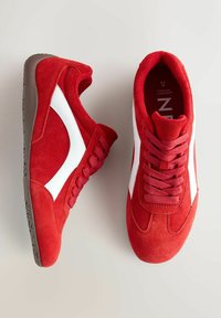 Bright red sneakers with white accents, featuring laces and a textured sole. Positioned on a light background, showcasing their style.