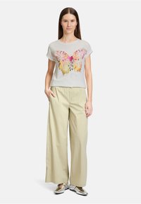 Lichtgrijze t-shirt met een kleurrijke vlinderprint, gecombineerd met beige, wijde broekspijpen en metallic zilveren schoenen. Eenvoudige, ontspannen pasvorm.