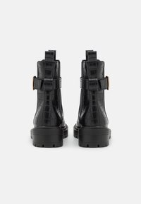 Botas de tobillo de cuero negro con relieve de cocodrilo, con un caña alta, correas ajustables y suelas de goma resistentes. Con un acabado mate.